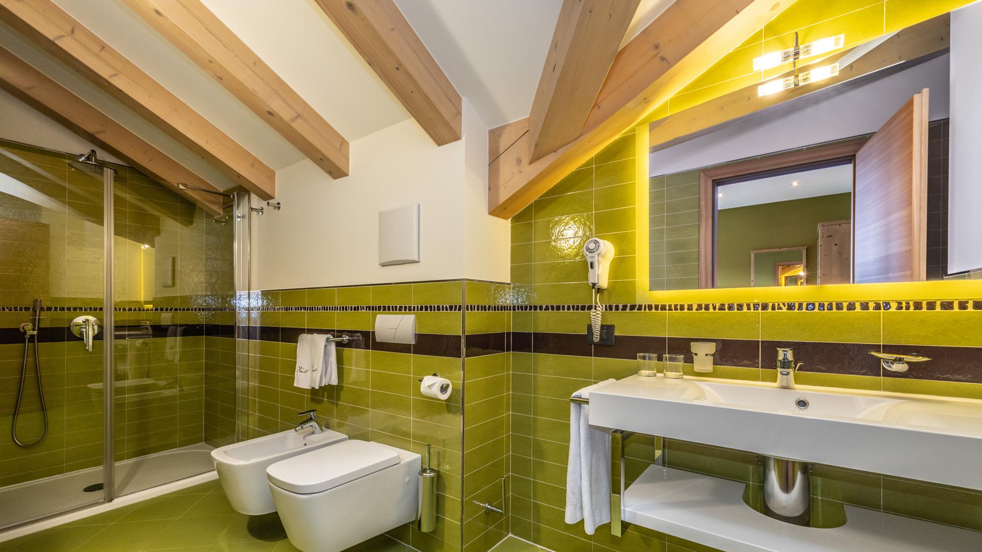 Bagno moderno con piastrelle verdi e soffitto con travi a vista.