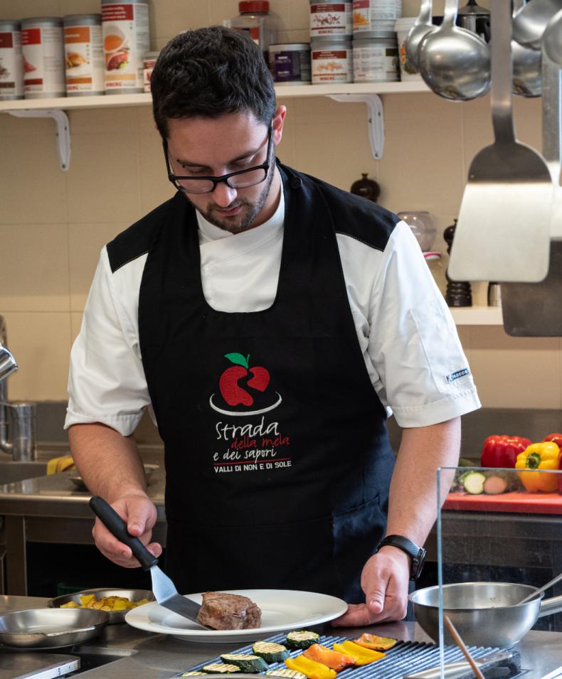 Chef prepara piatto con carne e verdure grigliate.